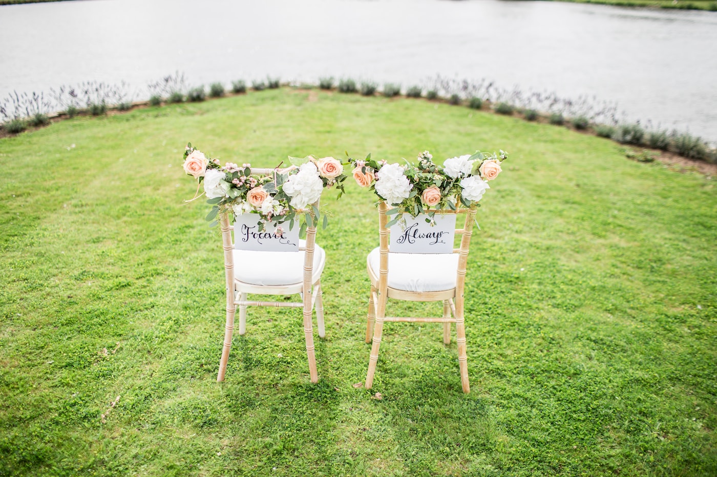 Decorated chairs set beside a waterside wedding aisle