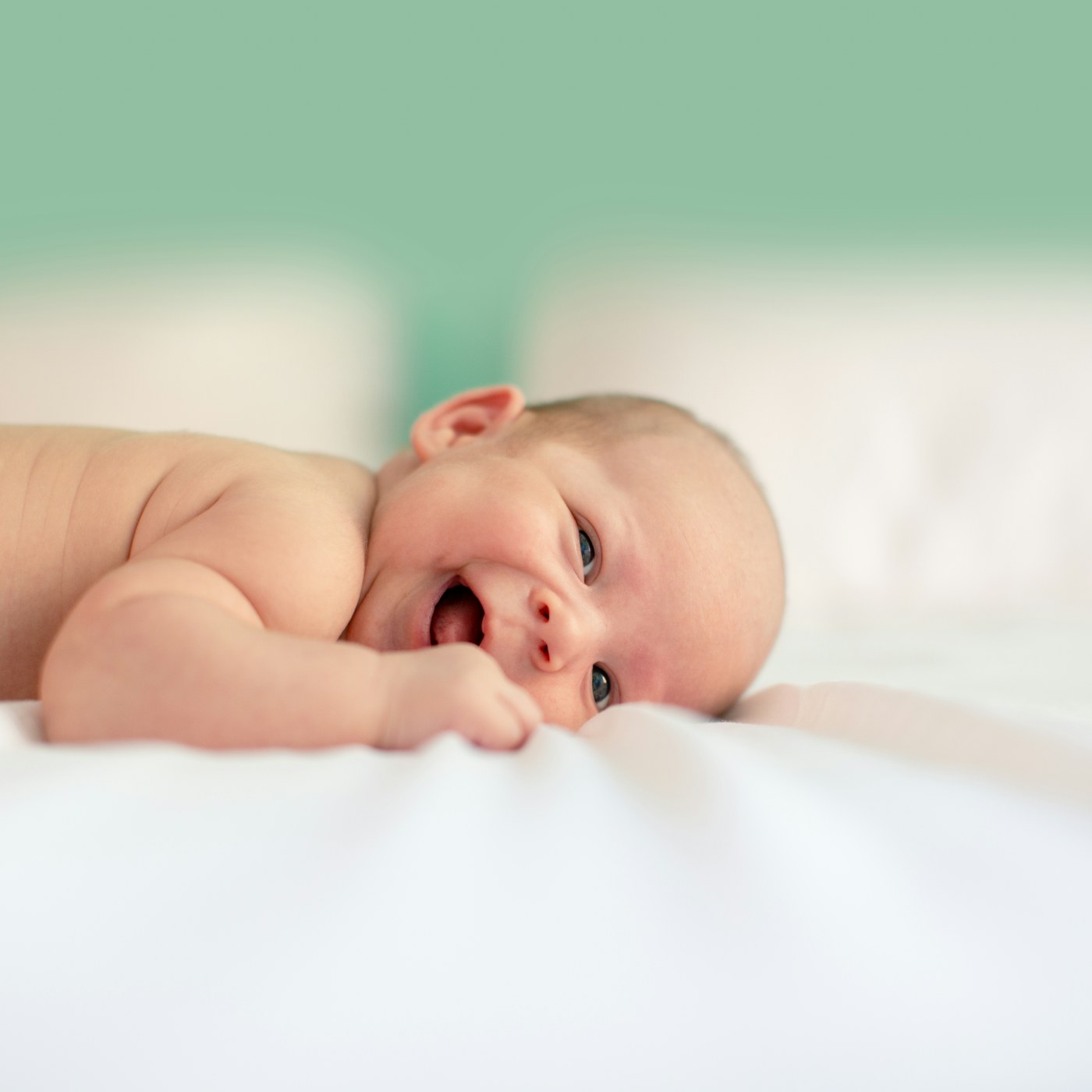 A smiling newborn lying on white bedding
