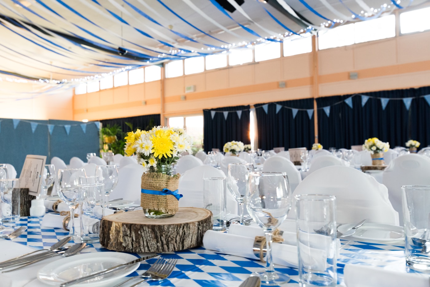 A reception hall with white-covered chairs around blue-patterned tables